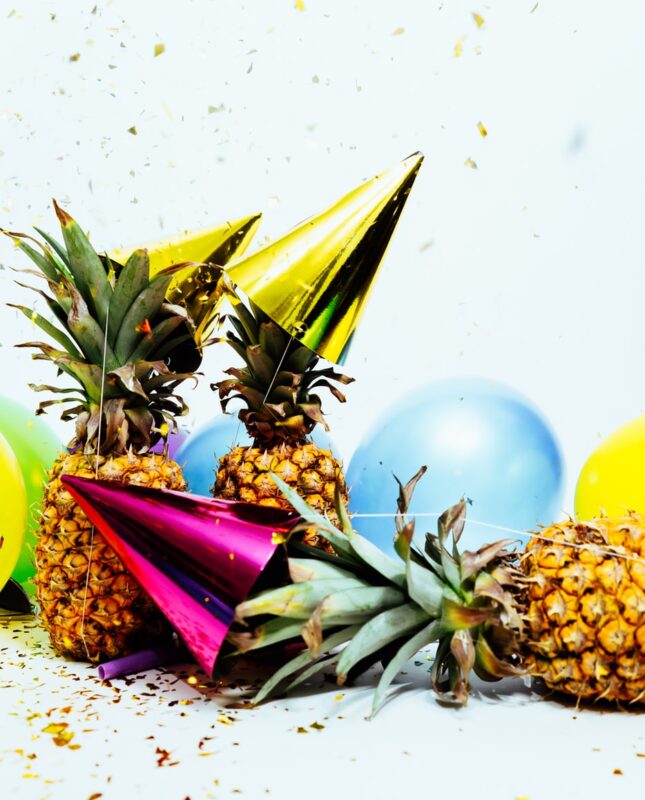 Bright party hats and balloons rests on pineapples.