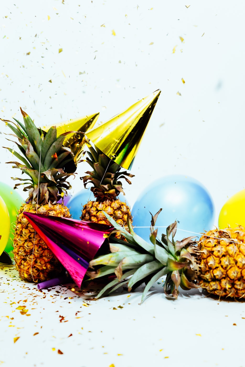 Bright party hats and balloons rests on pineapples.